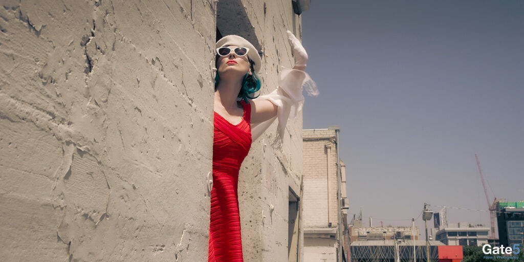 a french woman waves in a red dress from a door in a building